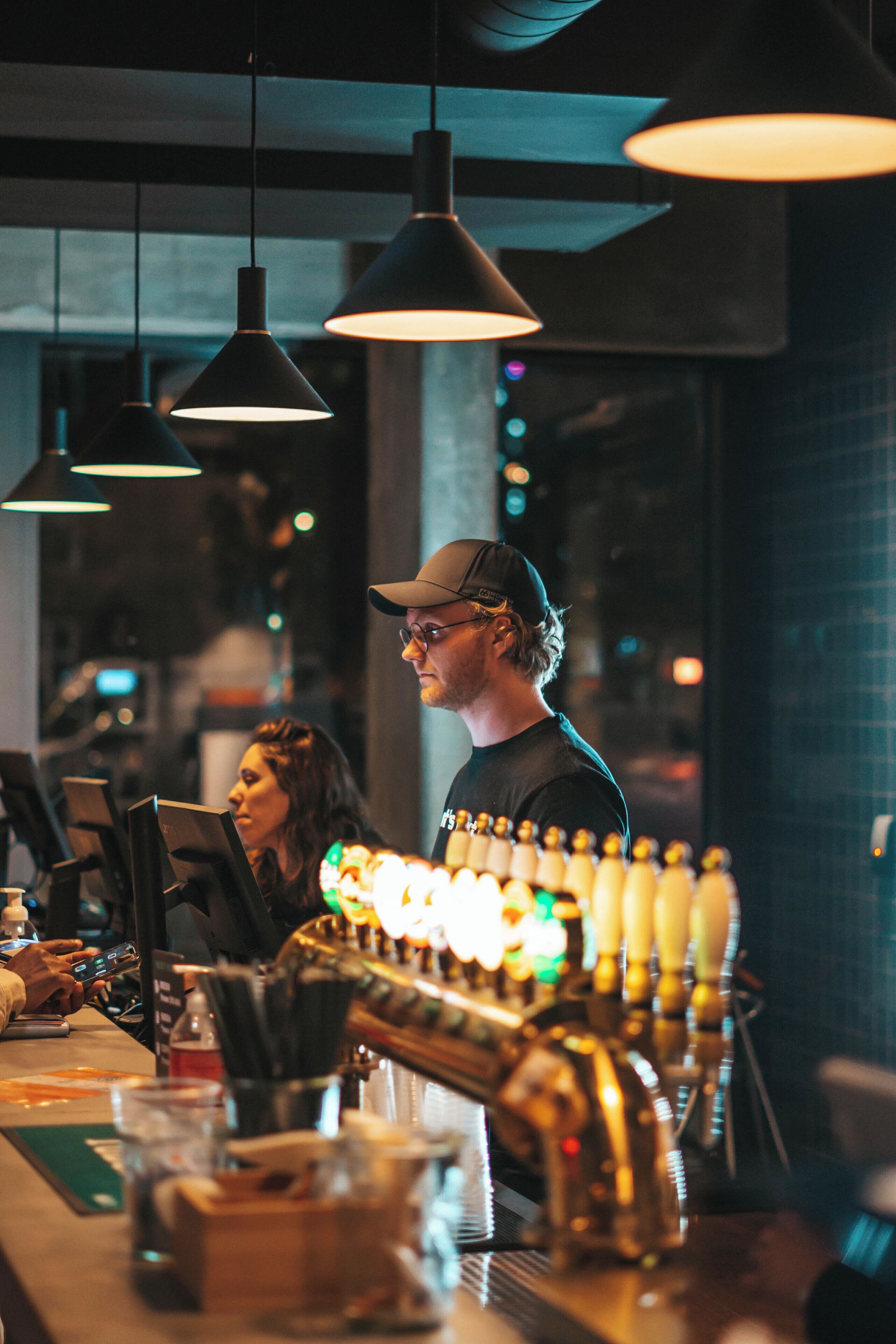 A bar with multiple hanging pendant lights, a bartender, and a customer.