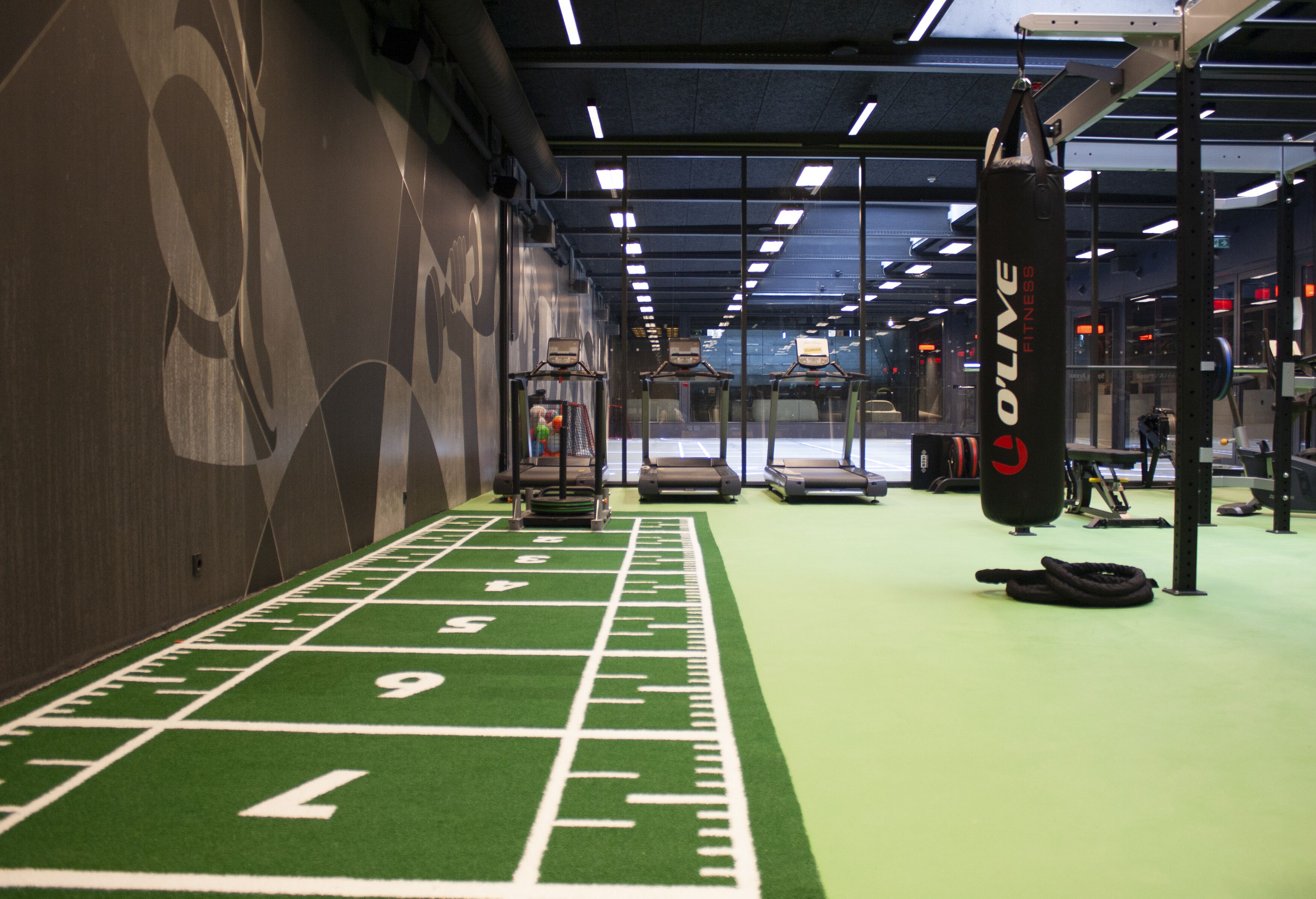 Een sportschool met een groen kunstgrasveld, krachttrainingapparatuur en een bokszak.