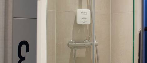 Ducha con panel de control etiquetado como "Next House" y puerta de vidrio.
