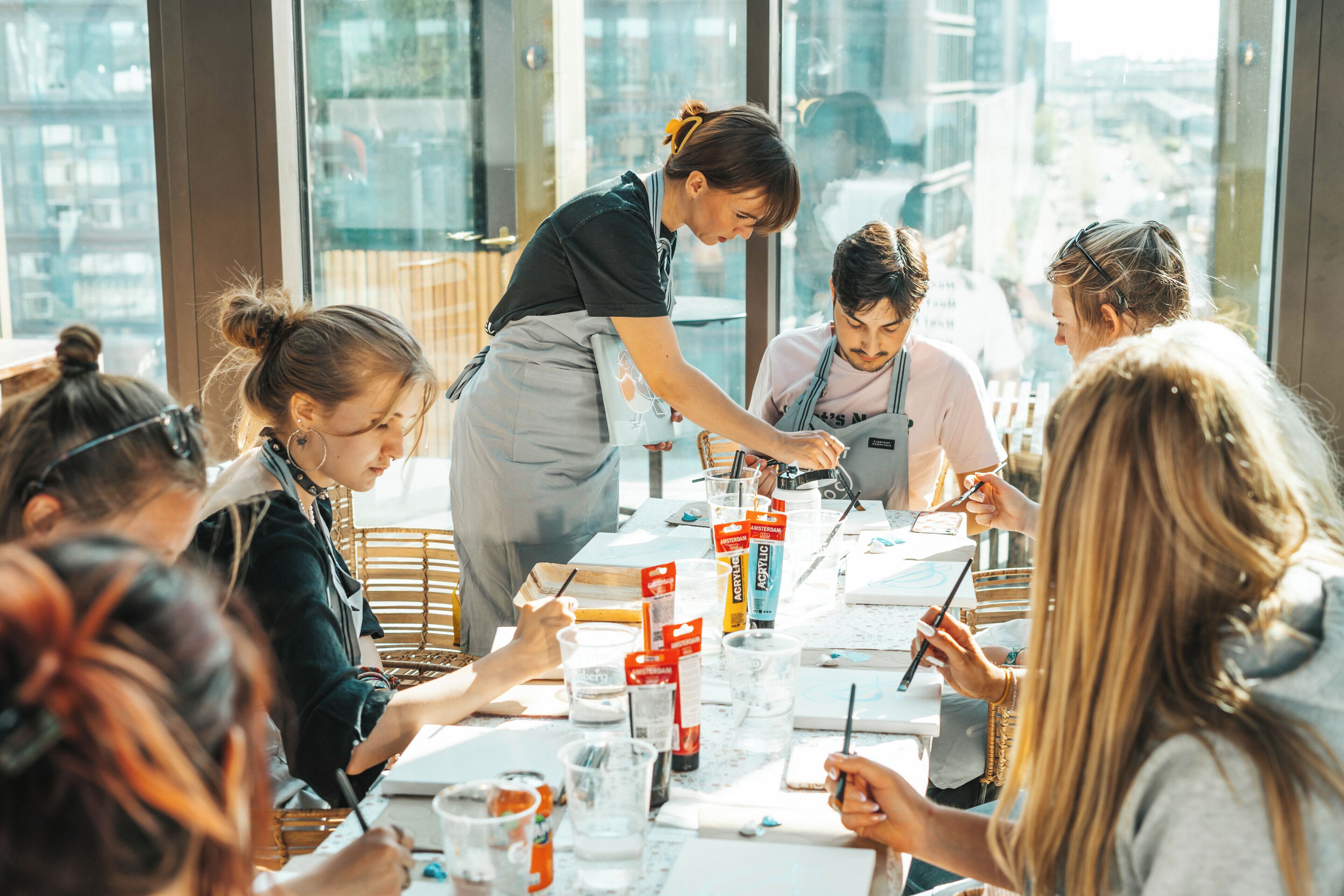 A group of people engaged in a painting activity around a table with art supplies.