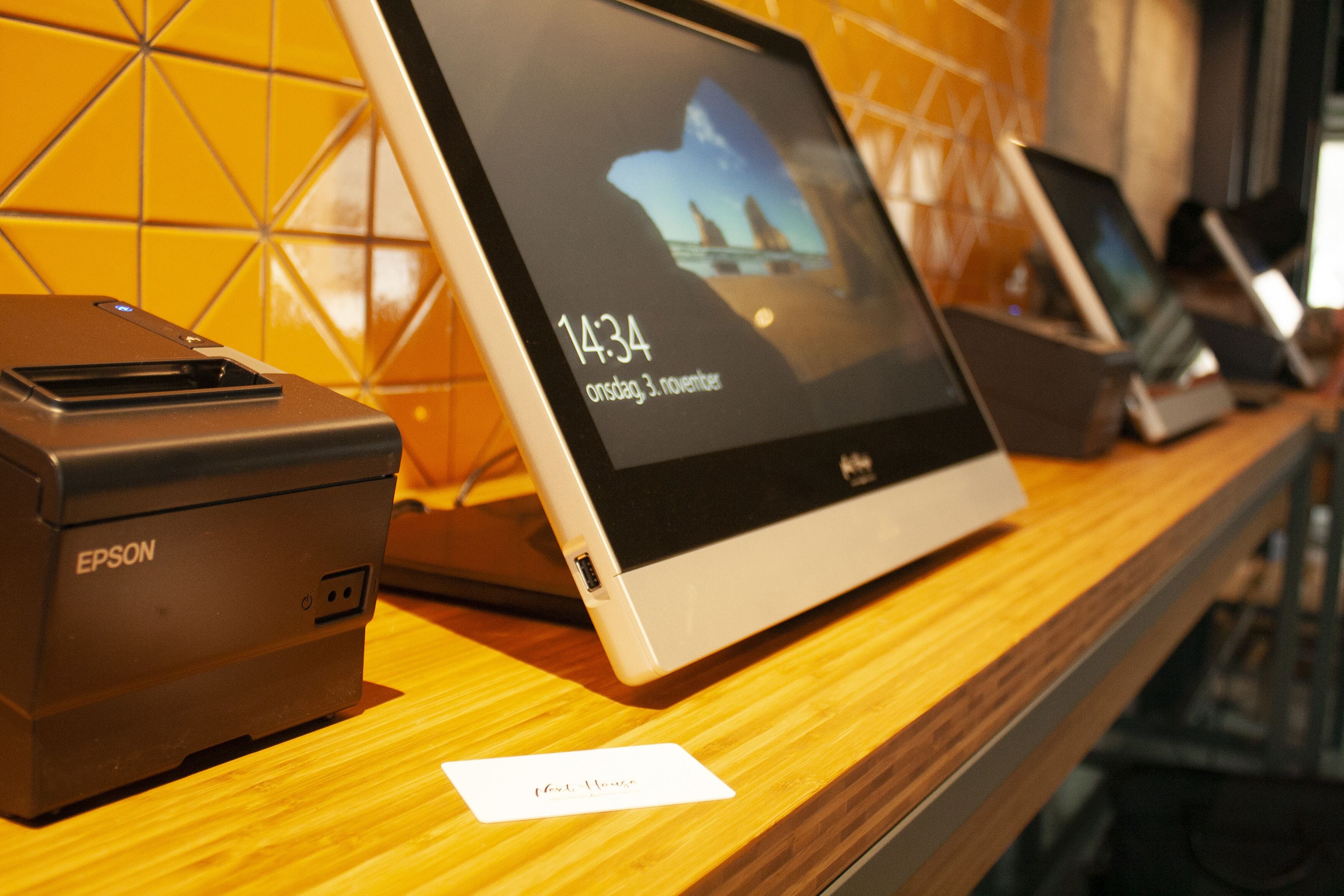 A digital display with a date and time, a printer, and a card on a wooden surface.