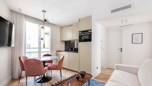 A modern kitchen with white cabinets, a built-in oven, and a dining area with pink chairs and a round table. - St Georges - Fabulous Two Bedroom in Paris (Paris)
