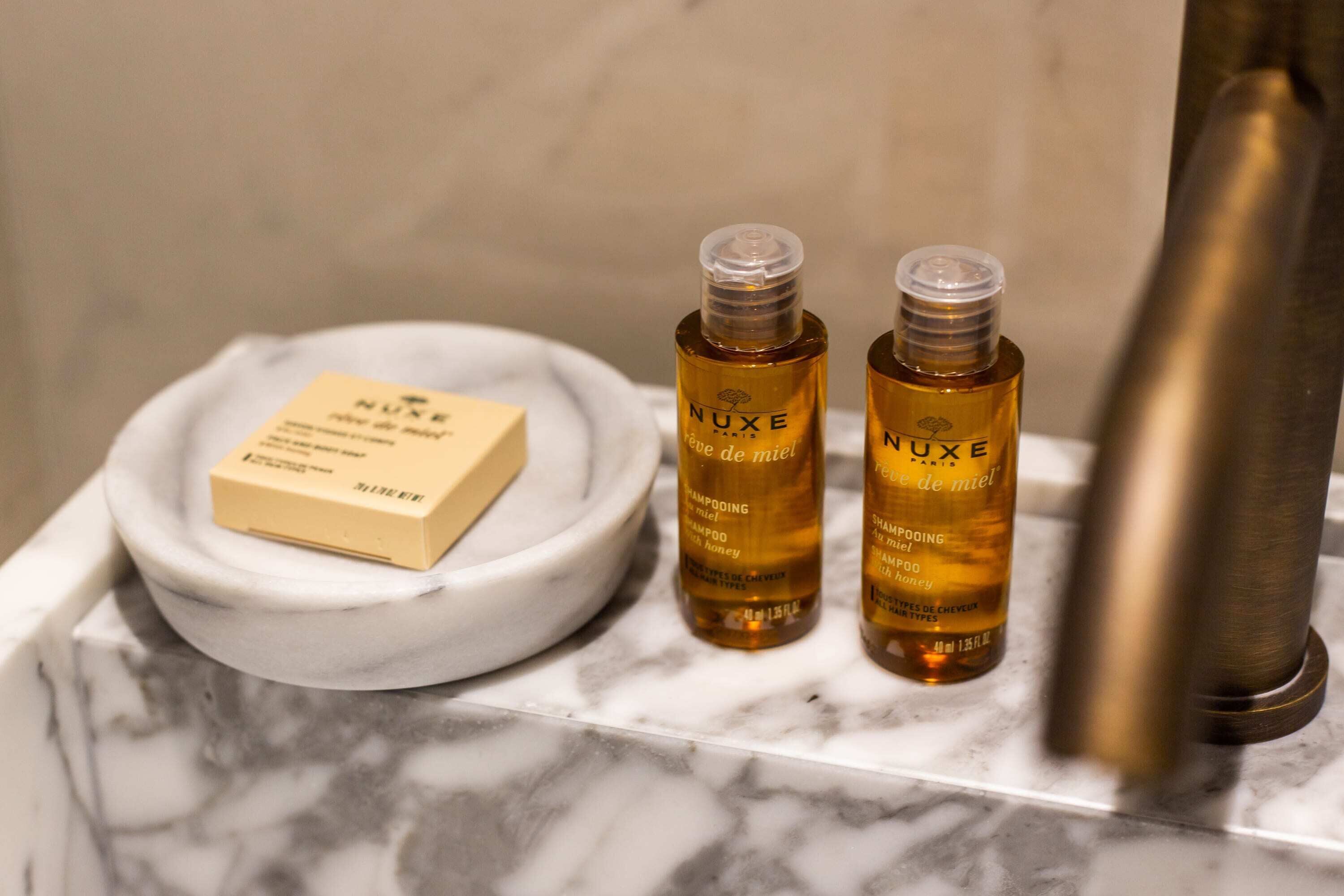 Une salle de bain avec un plan de toilette en marbre, deux flacons de shampoing NUXE et un porte-savon contenant un pain de savon.