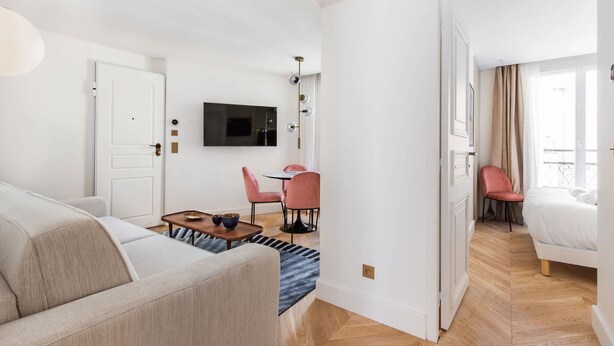 A modern hotel room with a sofa, a dining table with chairs, a TV mounted on the wall, and a bed with a view. - St Georges - Superb 3 Bedroom (Paris)