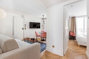 Quarto de hotel moderno com sofá, mesa de jantar com cadeiras, TV na parede e cama com vista.