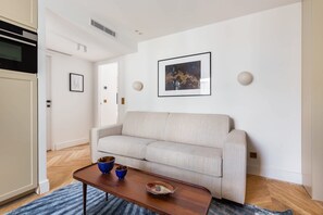 Un salon moderne avec un canapé beige, une table basse en bois agrémentée de bols décoratifs et un tableau abstrait encadré accroché au mur.