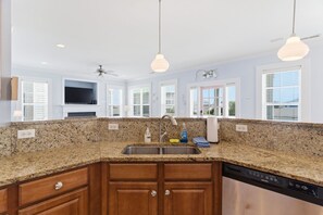 A kitchen with granite countertops, wooden cabinets, a stainless steel sink, and pendant lighting.