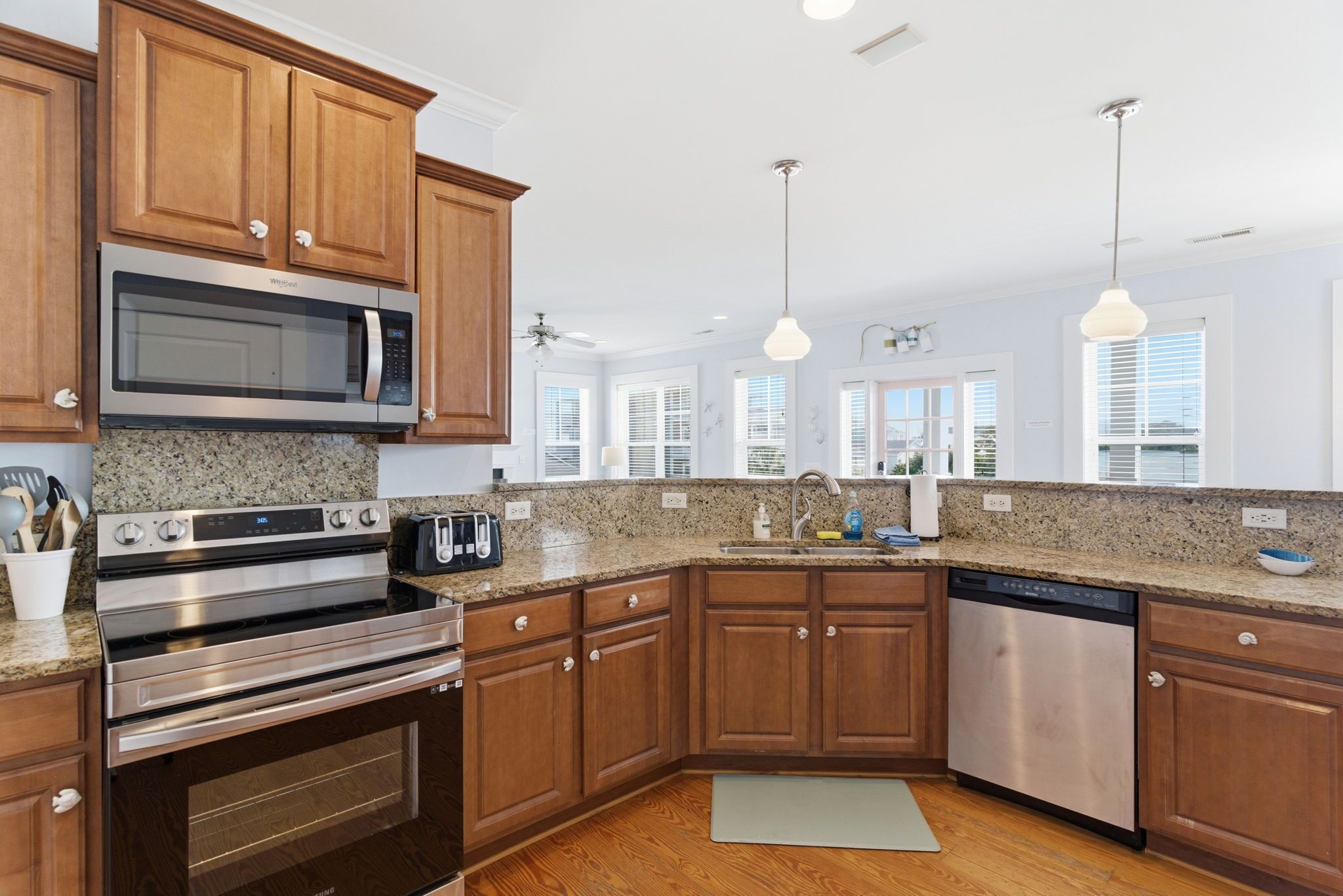 A modern kitchen with wooden cabinets, stainless steel appliances, granite countertops, and pendant lighting.