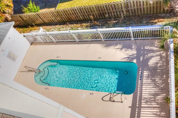A rectangular swimming pool with a white deck and a wooden fence in the background. - Clam Shack - Oceanview and waterway view townhome, elevator, pool! (Carolina Beach)