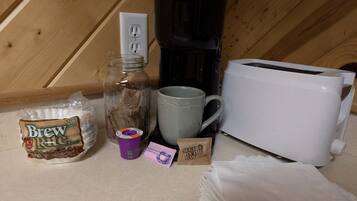A kitchen counter with a coffee maker, a toaster, a mug, a jar, a bag of coffee, and a packet of tea.