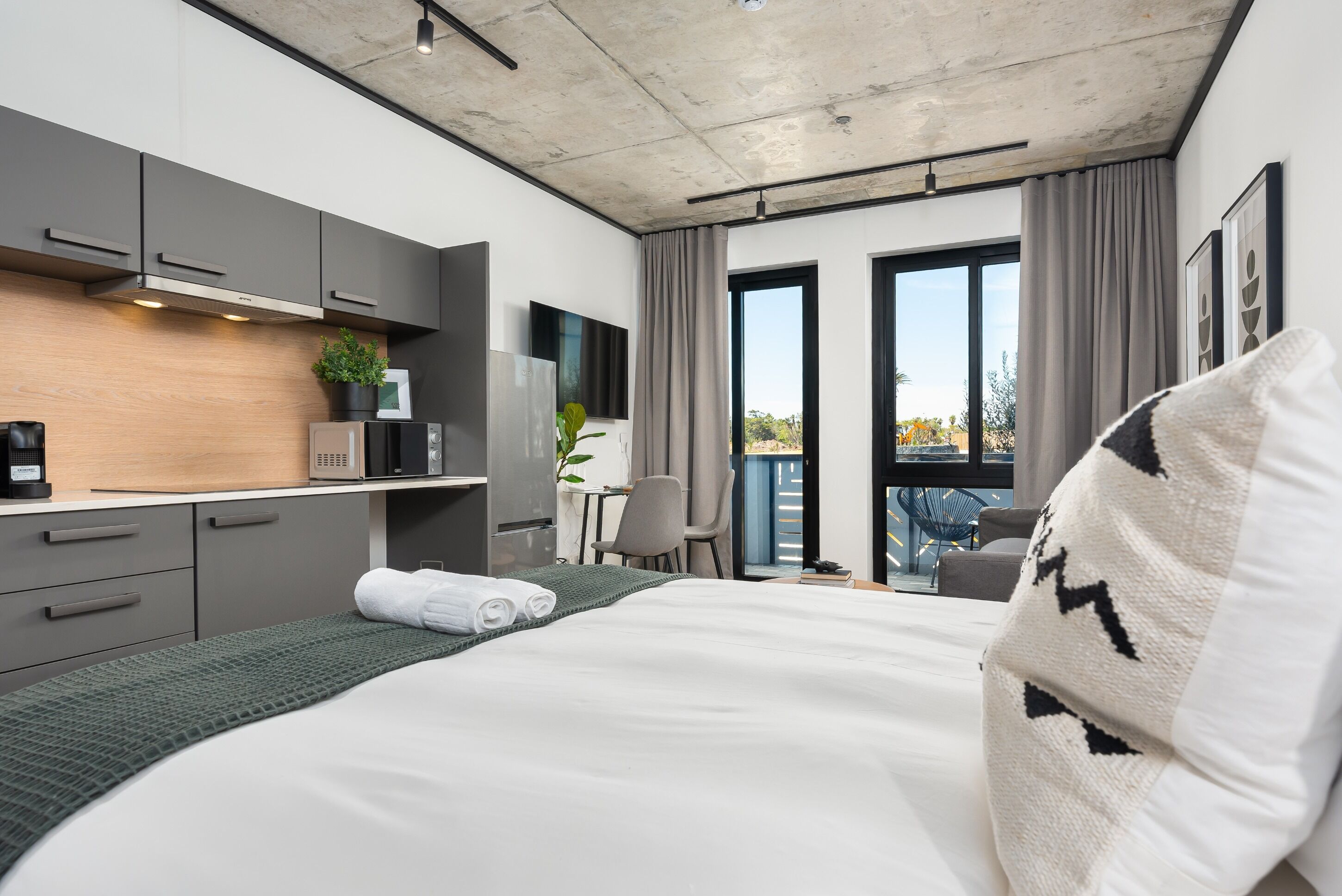 Una habitación de hotel moderna con una cama grande, un escritorio, un televisor de pantalla plana y un balcón con vistas.