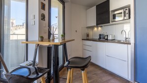 A compact kitchen with a microwave, toaster, and sink. There is a small table with two stools and a potted plant. - Terrasse en ville - Première conciergerie (Montpellier)