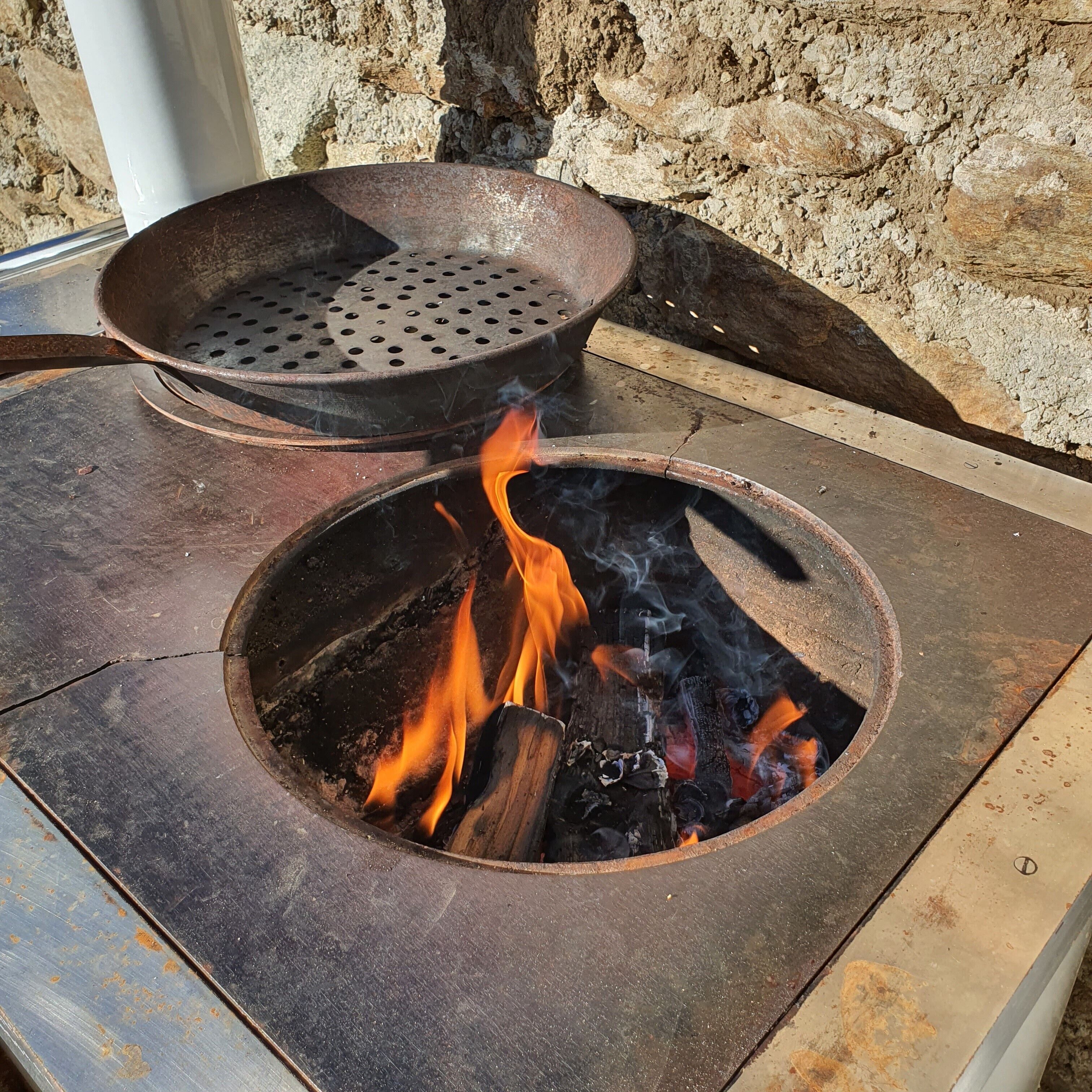 Un foyer extérieur en métal, doté d’une ouverture circulaire et d’un plateau en métal perforé sur le dessus.