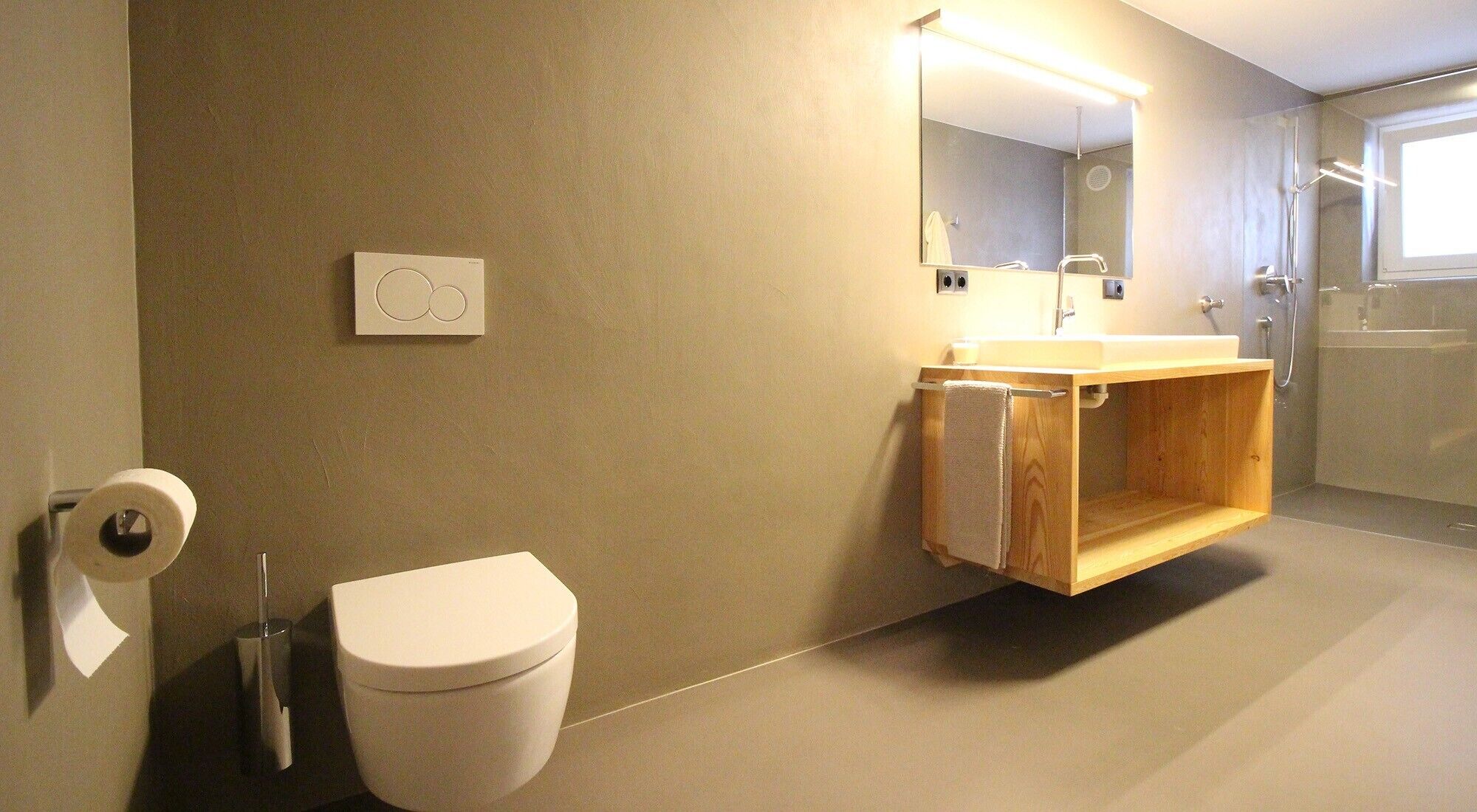 A modern bathroom with a toilet, a wooden vanity, a mirror, and a shower area.