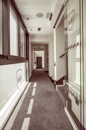Un couloir avec un tapis à motifs, des portes en verre ornées d’un logo et un extincteur fixé au mur.