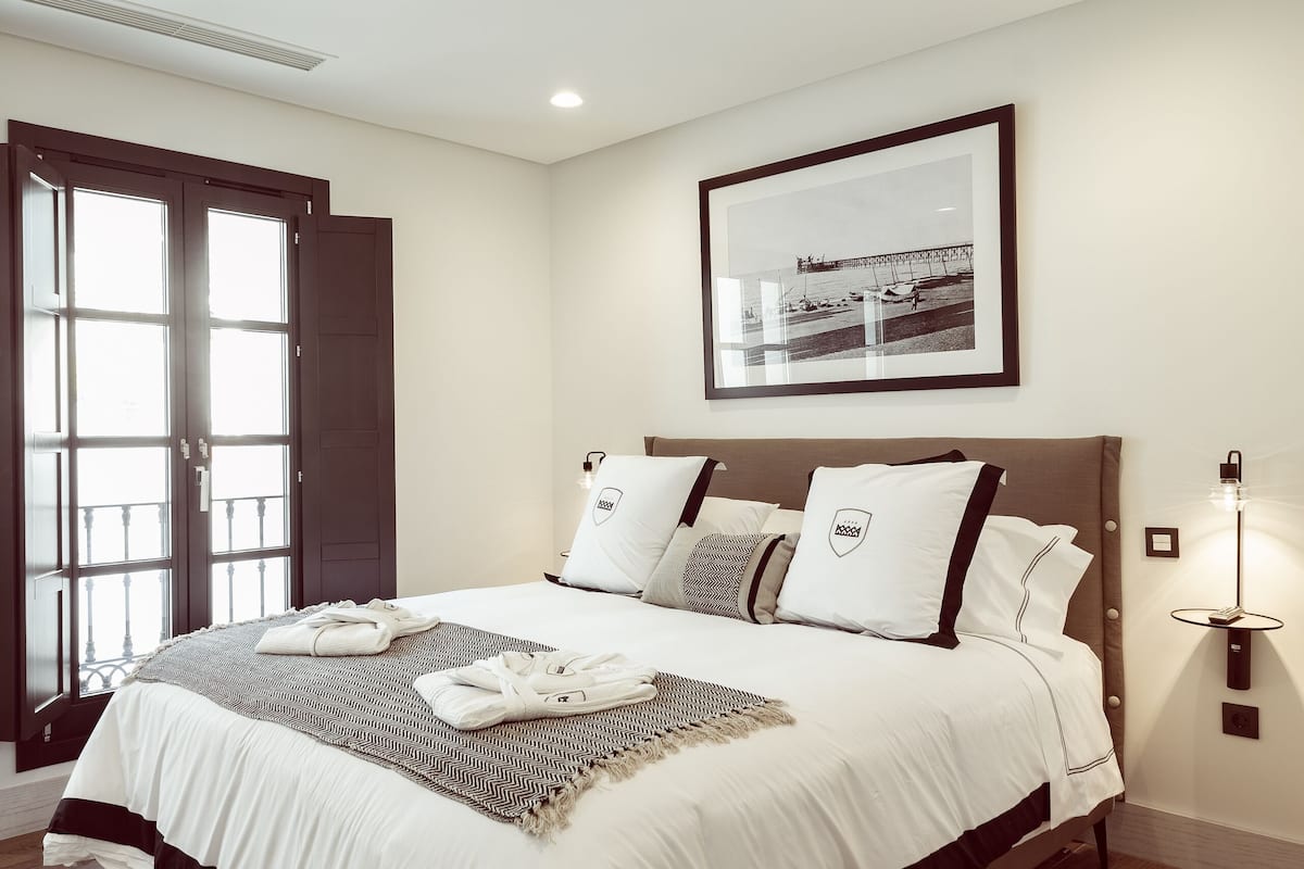 Una camera da letto ordinata con un letto grande, un quadro appeso al muro e una porta che dà su uno spazio esterno.