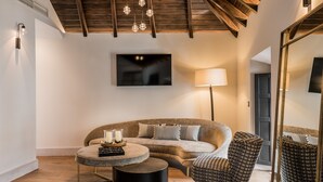 A modern living room with a sofa, two patterned chairs, a round coffee table, a floor lamp, and a flat-screen TV mounted on the wall. - Hotel Maison Ardois La Ciudadela Marbella (Marbella)
