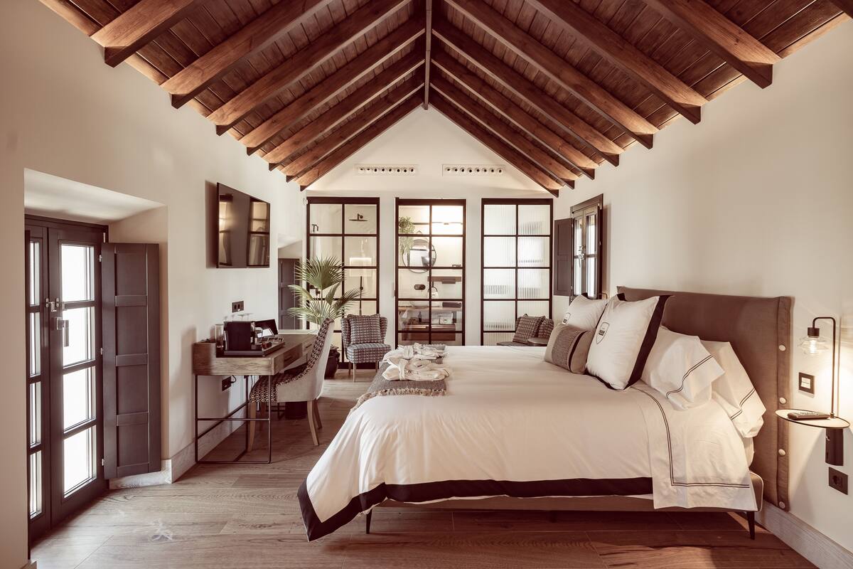 Una camera da letto con un letto grande, travi in legno a soffitto, una scrivania con una sedia e una finestra con vista.