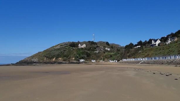 Une plage avec un ciel dégagé, un phare et des maisons sur une colline.