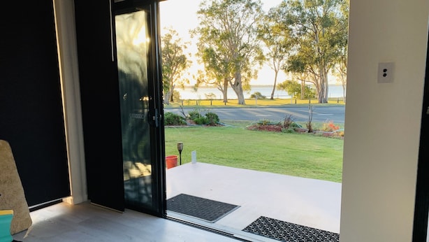 A room with a sliding glass door leading to a balcony with a view of a grassy area and trees. - Water front Property with magical sunsets and water front walking and bike paths (Banksia Beach)