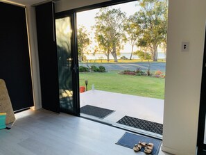 Een kamer met een schuifglazen deur die uitkomt op een balkon met uitzicht op een grasveld en bomen.