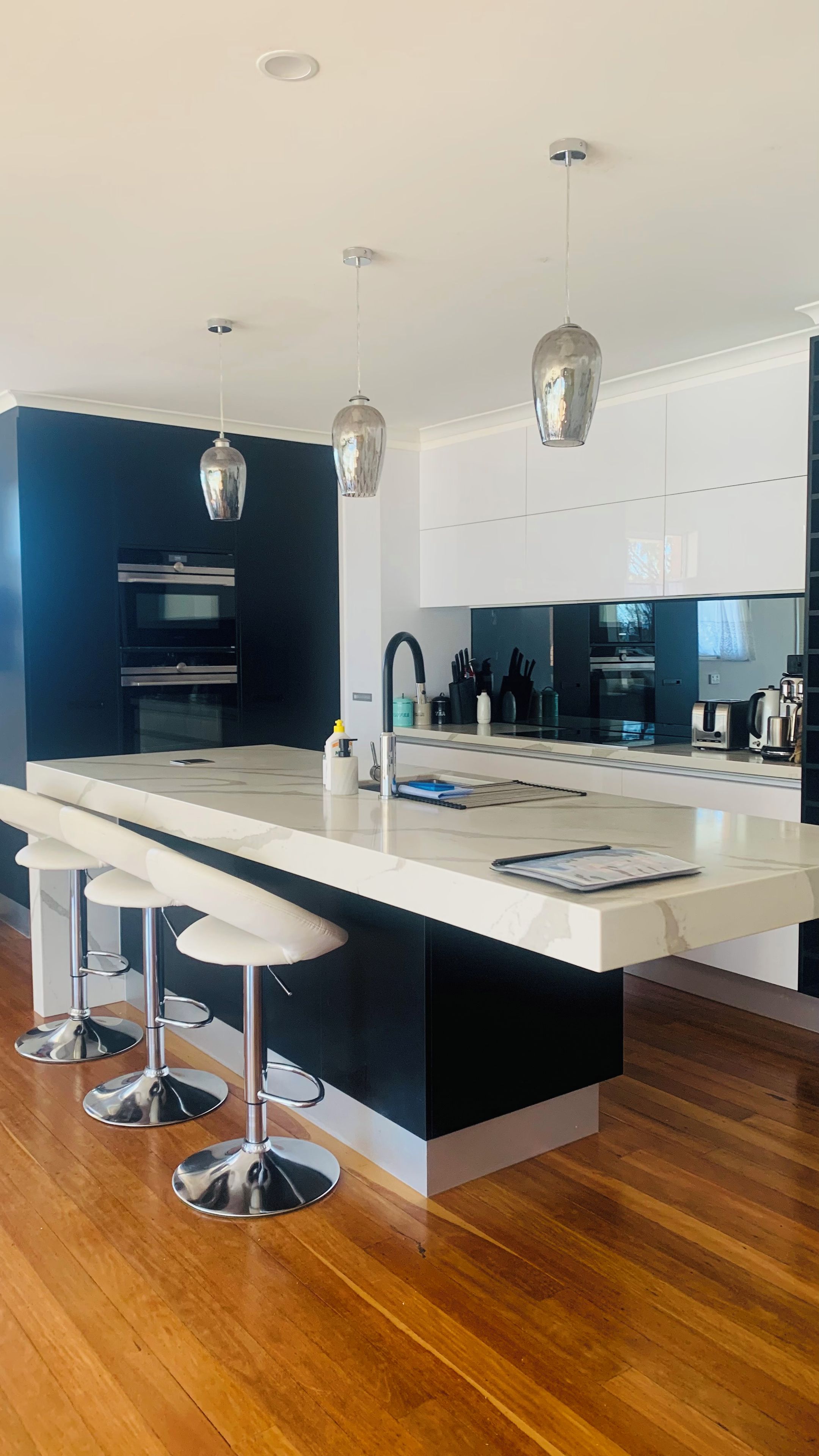 Una cocina moderna con una isla central, taburetes de bar, electrodomésticos de acero inoxidable e iluminación colgante.