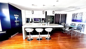 A modern kitchen with a central island, bar stools, and a dining area with patterned chairs. - Water front Property with magical sunsets and water front walking and bike paths (Banksia Beach)