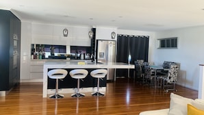 A modern kitchen with a central island, bar stools, a dining area with patterned chairs, and a refrigerator. - Water front Property with magical sunsets and water front walking and bike paths (Banksia Beach)