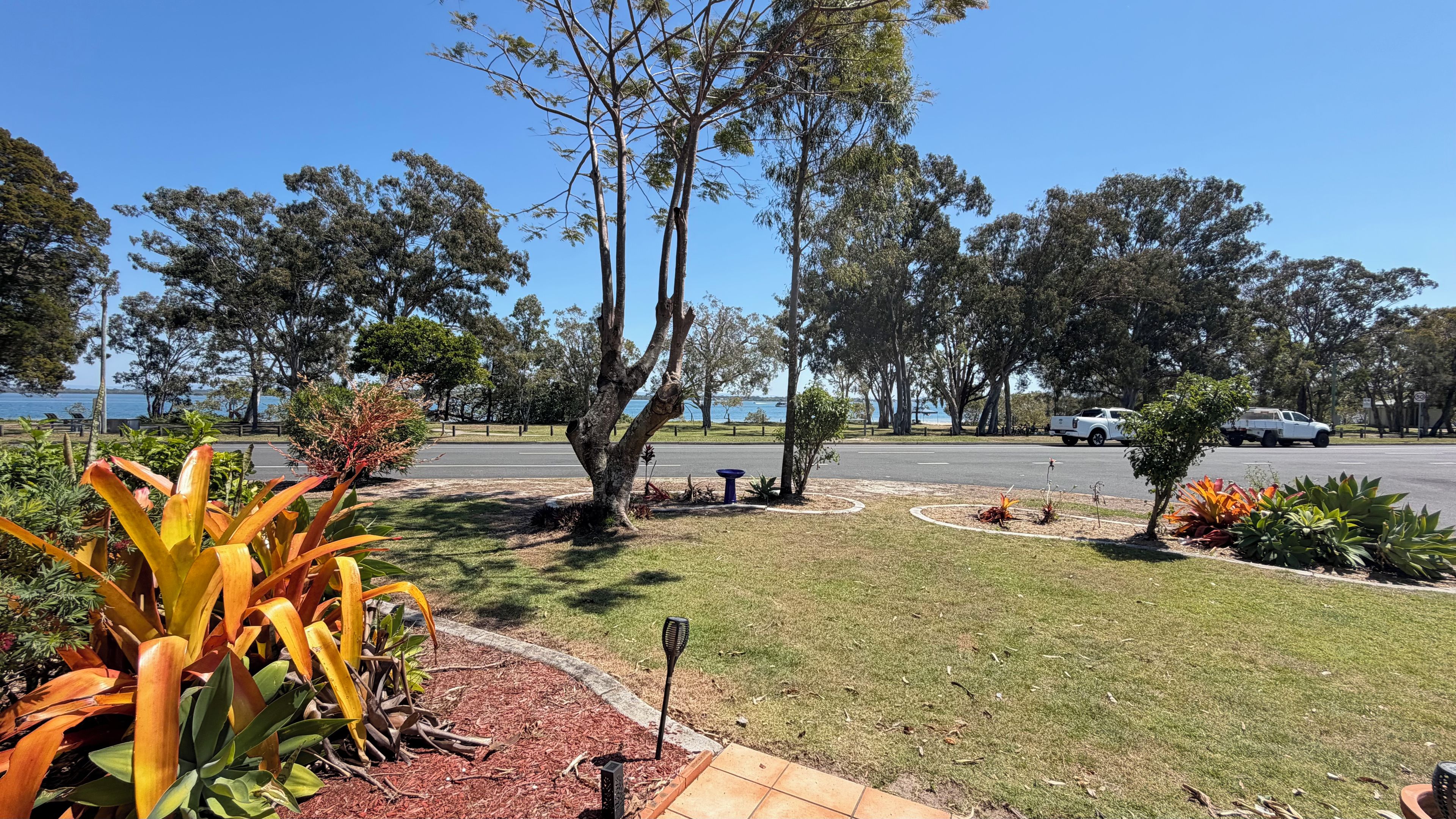 A landscaped area with a lawn, trees, and a road with vehicles.