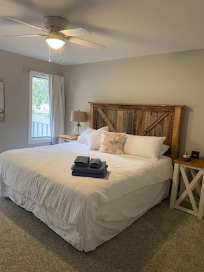 Une chambre à coucher avec un grand lit, une tête de lit en bois, un ventilateur de plafond et une table de chevet avec une lampe.