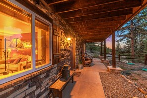 A covered porch with stone walls, a seating area with a sofa and chairs, and a view of the surrounding landscape.