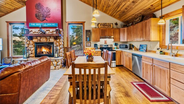 A cozy interior with a stone fireplace, wooden ceiling, and a dining area with a view of the outdoors.