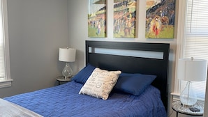A bedroom with a bed, a nightstand, a lamp, and three paintings on the wall. - The Steel City Loft  (Bethlehem)