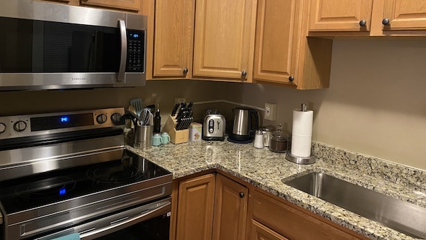 A kitchen with wooden cabinets, stainless steel appliances including a microwave, oven, and toaster, and granite countertops. - The Steel City Loft  (Bethlehem)