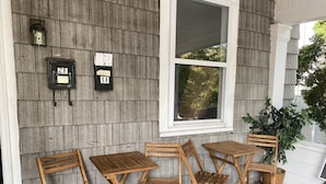 A porch with wooden folding chairs and tables, a mailbox, and a window with a view of trees. - The Steel City Loft  (Bethlehem)