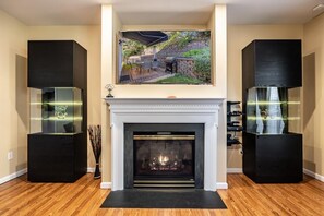 A living room with a fireplace, a large framed picture above it, and two black speakers on either side.