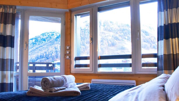 A bedroom with a bed, a window with a view of a snowy mountain, and a door leading outside.