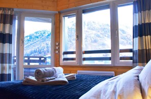 A bedroom with a bed, a window with a view of a snowy mountain, and a door leading outside.