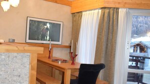 A cozy room with a wooden desk, a chair, a television, and a large window with curtains.