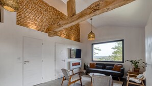 A modern living room with exposed brick walls, a large window, and a cozy seating area. - Villa Kundalini - Three Bedroom Villa, Sleeps 8 (Ambres)