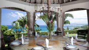 A dining area with a table set for four, a chandelier, and a view of the ocean.