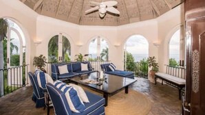A spacious patio with blue and white striped furniture, a ceiling fan, and a view of the ocean.