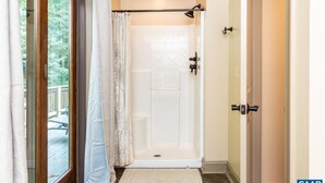 Een douche met een glazen deur, een witte douchegordijn en een klein vloerkleed.