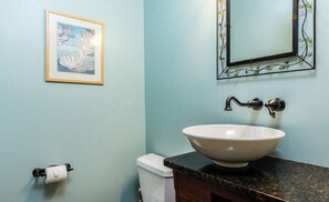 Un baño con un lavamanos blanco, una obra de arte enmarcada en la pared y un inodoro con un rollo de papel higiénico.