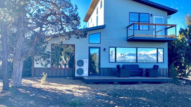A modern two-story house with a balcony, large windows, and a view of mountains.