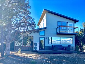 Ett modernt hus i två våningar med en balkong, stora fönster och utsikt över bergen.