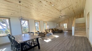 A spacious room with a wooden ceiling, a dining area with a long table and chairs, a sofa, and a staircase.