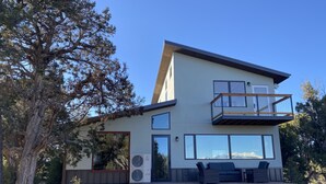 A modern two-story house with a balcony, large windows, and outdoor furniture.