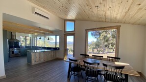 A spacious kitchen with a large island, wooden ceiling, and large windows offering a view of the outdoors.