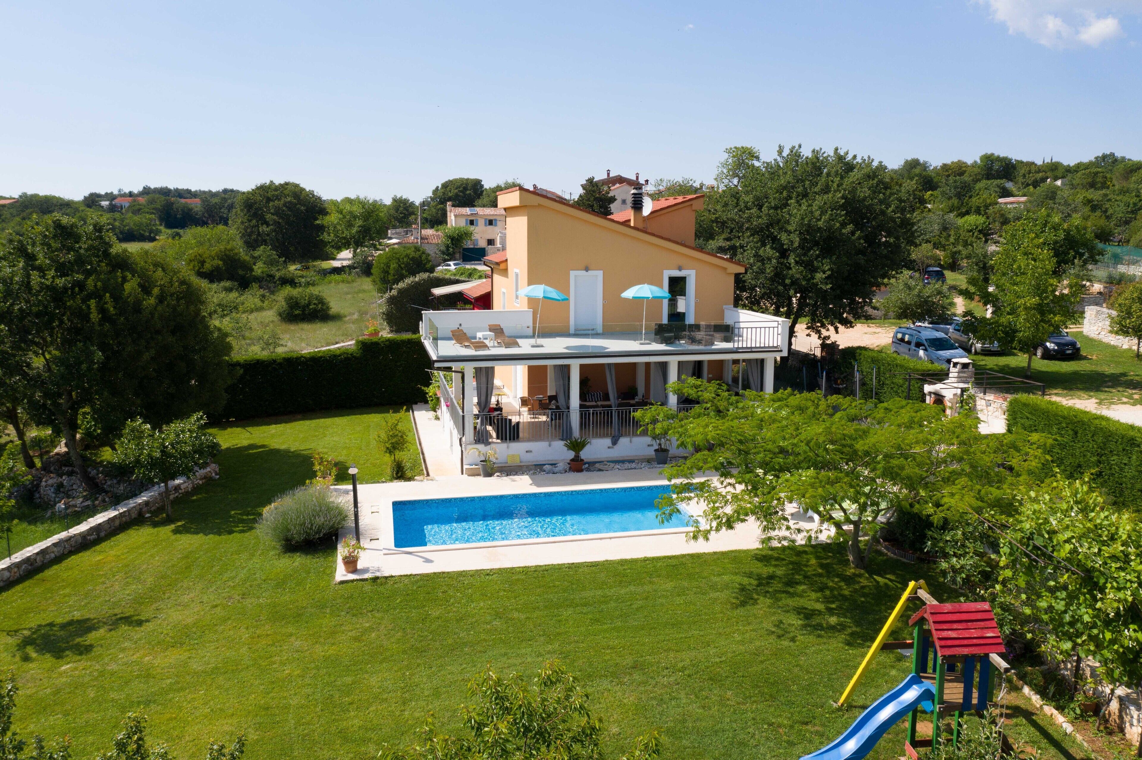 A two-story house with a swimming pool, a patio with outdoor furniture, and a playground.